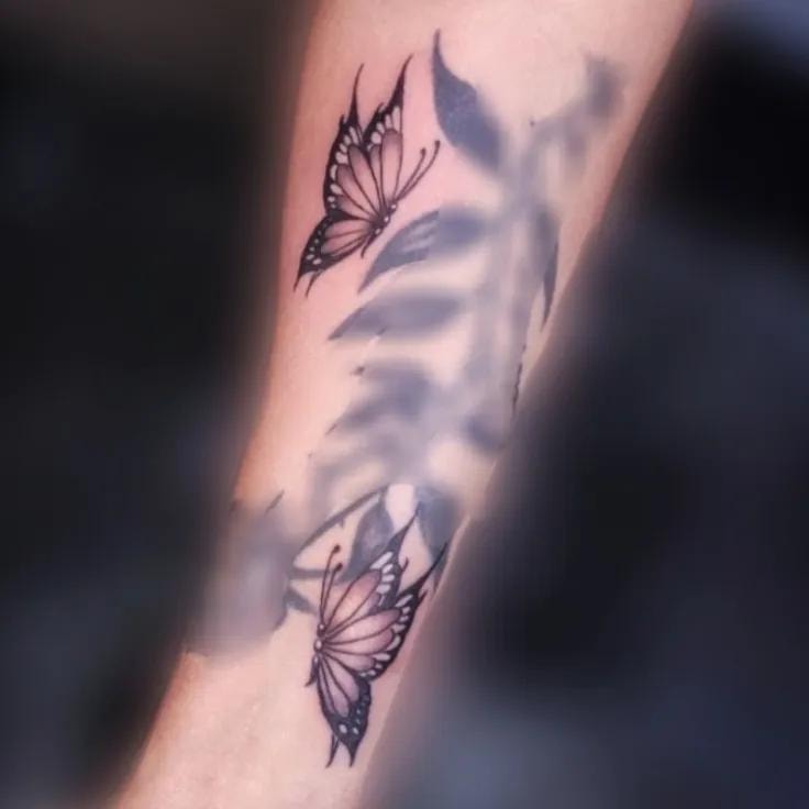 Dos mariposas con hojas tatuadas en el antebrazo